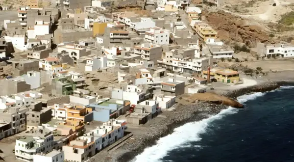 Vista aérea de un pueblo costero en las maretas Tenerife, con casas blancas y de colores apiladas en una ladera rocosa junto al mar azul.