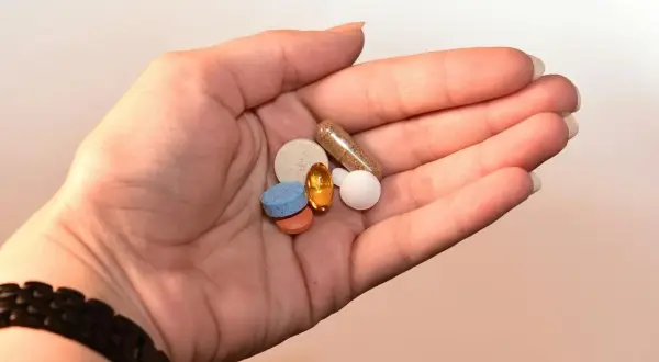 Dłoń trzyma garść pigułek i kapsułek, które mogą pomóc w regulacji nastroju, np. przy zespole serotoninowym.