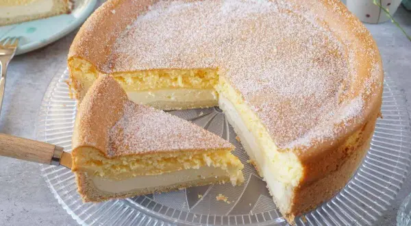 Saftige eierschecke ohne boden, mit Puderzucker bestäubt, auf einem Tortenteller. Ein Stück wurde bereits herausgeschnitten.