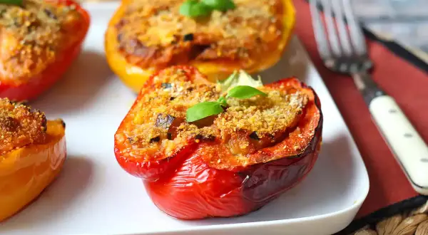 Poivrons farcis colorés, dorés et appétissants, garnis d'une chapelure croustillante et d'une feuille de basilic frais.