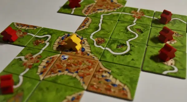 Rozgrywka w Carcassonne: czerwoni i żółci rycerze zajmują pola z miastami i drogami, budując średniowieczny krajobraz.