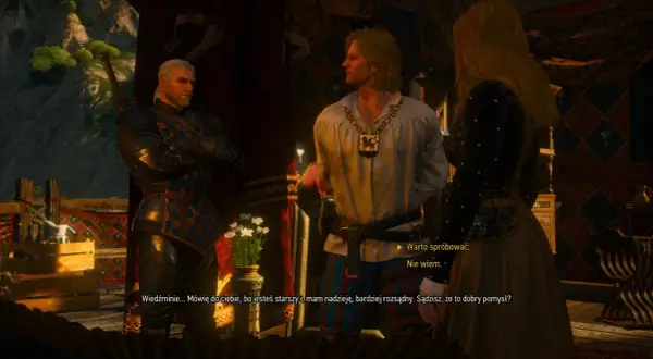 Geralt z Rivii w zbroi rozmawia z młodym mężczyzną i kobietą. W tle widać wnętrze karczmy w Wiedźmin 3.