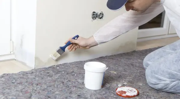 Maler streicht mit Pinsel über Wasserflecken an der Wand, um sie zu überdecken.