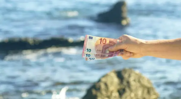 Dłoń trzyma banknoty euro na tle morza. Czarnogóra walutą i językiem jest w Europie.