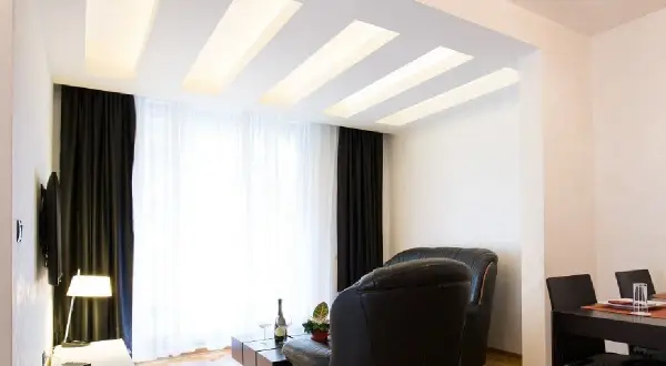 Nowoczesny salon z designerskim plafonem led, który subtelnie rozświetla wnętrze. Drewniane elementy dodają ciepła.