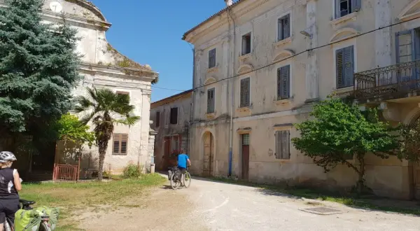 Ciclistas exploran un pueblo antiguo en Croacia, con edificios de piedra y vegetación exuberante.