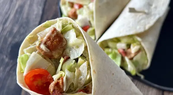 Pyszna tortilla z kurczakiem, chrupiącą sałatą, pomidorkami i kremowym sosem. Idealna na szybki lunch.