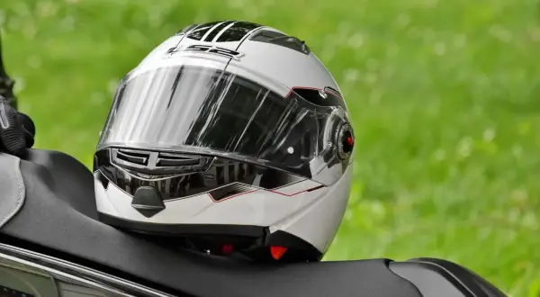 Biały kask motocyklowy z czarnymi i czerwonymi detalami leży na siedzeniu motocykla.