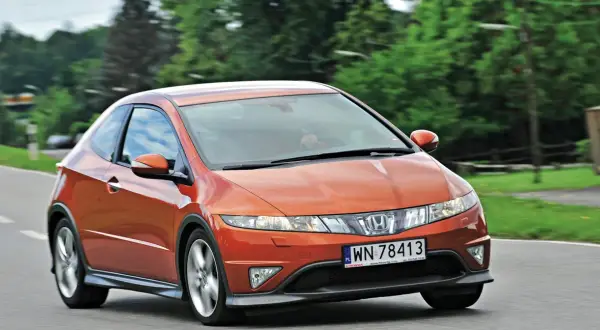 Pomarańczowy Honda Civic 8 tuning na drodze, z zielonymi drzewami w tle.