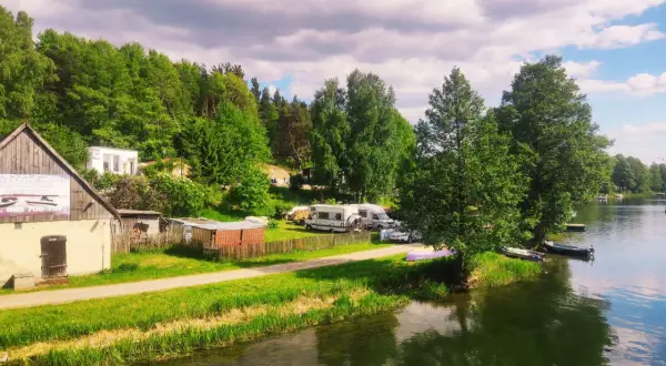 Malowniczy widok na jezioro i lasy, gdzie leżą Bory Tucholskie. Kemping z kamperami i łodziami przy brzegu.