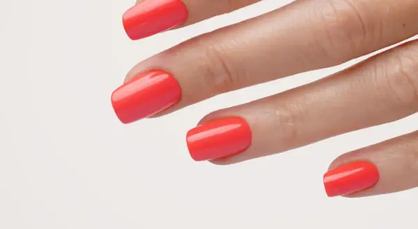 Main d'une femme avec un vernis corail vif, parfait pour un ongle vacances.