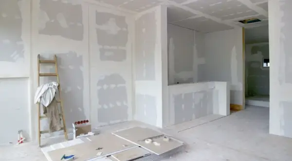 Interni in fase di finitura, con pareti in cartongesso pronte per essere stuccate. Una scala appoggiata al muro, pannelli e attrezzi a terra suggeriscono come fare un muro.