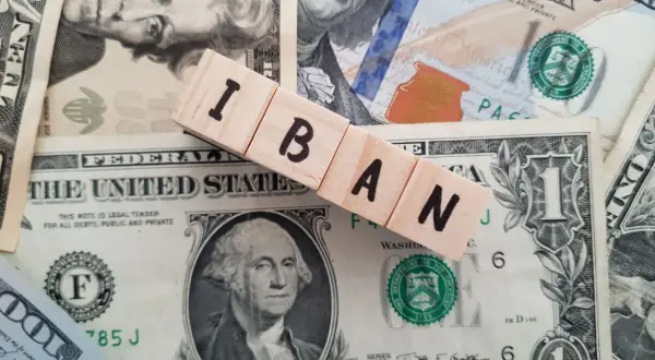 Drewniane klocki z napisem IBAN leżą na banknotach dolarowych. Dowiedz się, jak sprawdzić IBAN.