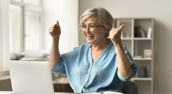 Szczęśliwa kobieta z kciukami w górze, cieszy się z pomyślnej odprawy emerytalnej online.