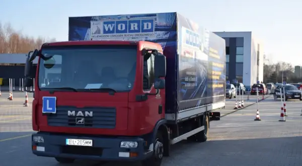 Czerwona ciężarówka MAN z literą "L" na masce, przygotowana do egzaminu na prawo jazdy kategorii C+E. Na naczepie logo WORD.
