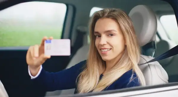 Uśmiechnięta młoda kobieta w samochodzie pokazuje swoje nowe prawo jazdy. Zdjęcie do prawa jazdy uszy są widoczne.