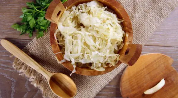 Holzschale mit Sauerkraut, daneben ein Holzlöffel und Petersilie. Sauerkraut gesund und lecker!