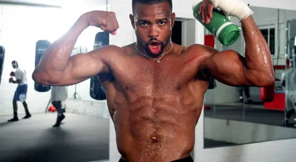 A sweaty boxer flexes his biceps in a gym, holding a green water bottle. He's training hard, ready for any division, perhaps even the Roy Jones Jr. division.