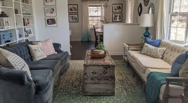 A living room with two sofas, a vintage trunk coffee table, and a patterned rug. This space shows how to brighten a dark room with light-colored furniture and ample natural light.