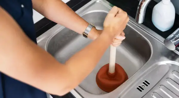 Une personne utilise une ventouse pour déboucher la canalisation d'eau chaude de l'évier.