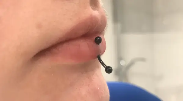 Zbliżenie na usta z czarnym kolczykiem typu vertical labret, który przechodzi pionowo przez dolną wargę.