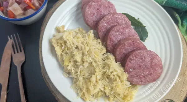 Piatto con fette di cotechino fresco e crauti, accompagnato da un'insalata di verdure e pane. Perfetto per la cottura.