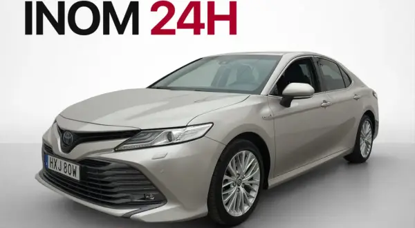 En silverfärgad, begagnad Toyota Camry hybrid visas framifrån. Hemleverans inom 24 timmar i Sverige.