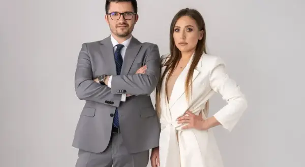Para prawników w garniturach, mężczyzna w szarym, kobieta w białym, na jasnym tle.