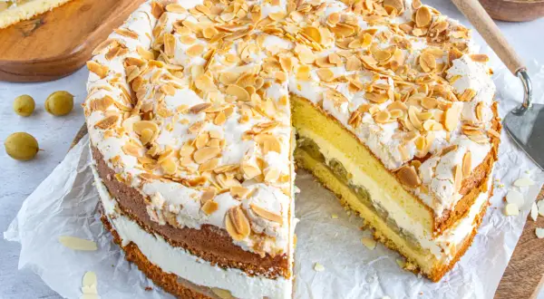 Eine köstliche Stachelbeer Baiser Torte, mit Baiserhaube und Mandelblättchen, daneben ein Stück Torte mit saftiger Füllung.