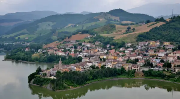 Borgo pittoresco affacciato su un lago, con case colorate e colline verdi sullo sfondo. Un gioiello nascosto nella regione di Urbino.