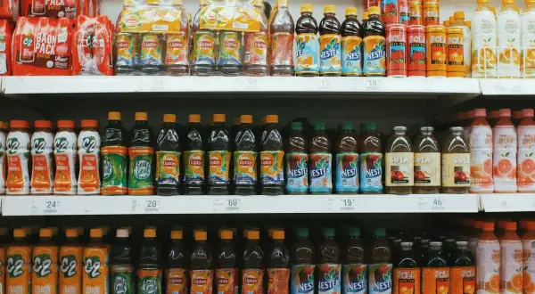 Rayons de supermarché remplis de bouteilles de thé glacé, de jus et de boissons. On y trouve des marques comme Lipton, Nestea et C2. Certaines bouteilles contiennent du bicarbonate dans l'eau pour une touche pétillante.