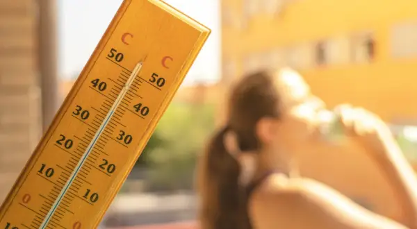 En termometer visar över 30 grader. En person dricker ur ett glas. Frågan är hur varmt får det vara på jobbet?