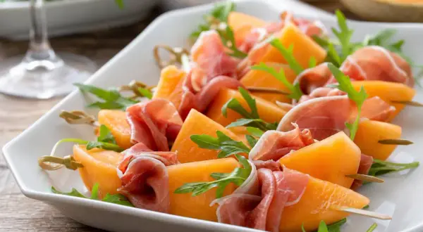 Melonenstücke mit Prosciutto und Rucola auf Spießen, perfekt als Snacks zum Wein.