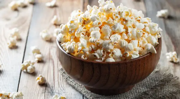 Drewniana miska pełna karmelowego popcornu na drewnianym tle.
