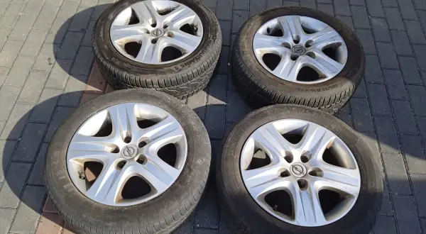Cztery felgi strukturalne Opel z oponami leżą na chodniku.