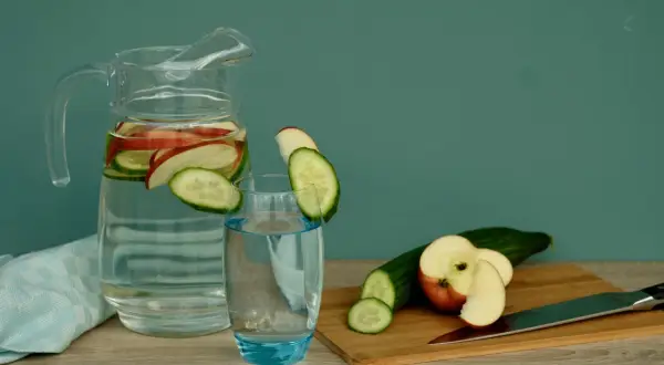 Erfrischendes Apfelwasser selber machen: Gurken- und Apfelscheiben in einer Karaffe und einem Glas.