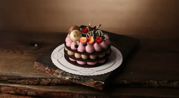 En vacker tårta med macarons, bär och chokladdekorationer, serverad på ett rustikt träfat.