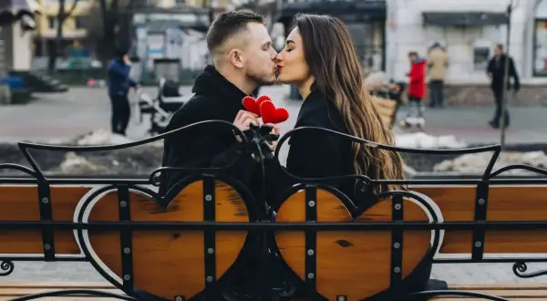 Para spędza romantyczny czas na ławce w kształcie serca, trzymając czerwone serduszka. To świetny pomysł, co można robić z chłopakiem poza domem.