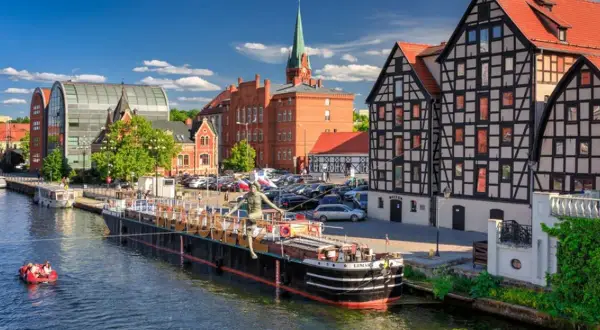 Malownicze stare miasta w Polsce nad rzeką. Barka z rzeźbą, łódka z ludźmi, zabytkowe kamienice i nowoczesna architektura.