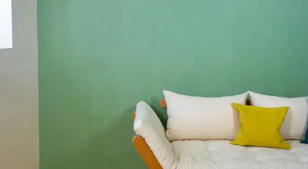 Ein Sofa mit weißen und gelben Kissen vor einer mintgrünen Wand. Die Frage "wieviel Wandfarbe pro qm" wird hier nicht beantwortet.
