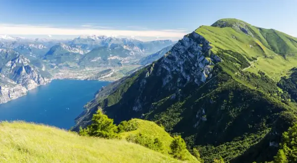 Panoramica mozzafiato dal Monte Baldo: lago blu intenso, montagne verdi e un cielo limpido.