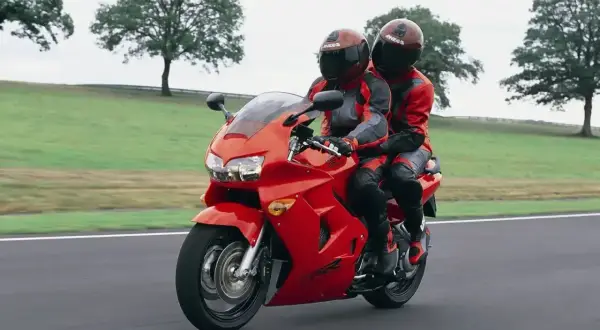 Dwie osoby w czerwonych kombinezonach jadą na czerwonym motocyklu Honda VFR 800.