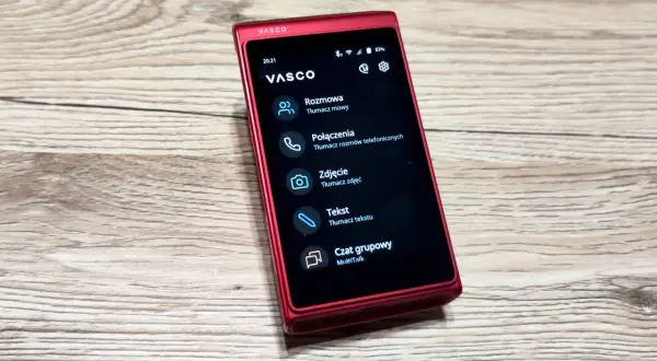 Czerwony translator głosowy Vasco na drewnianym blacie. Urządzenie oferuje tłumaczenie mowy, rozmów telefonicznych, zdjęć i tekstu.