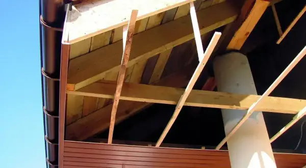 Widok od spodu na konstrukcję dachu z widoczną podprzybitką, rynną i kominem.