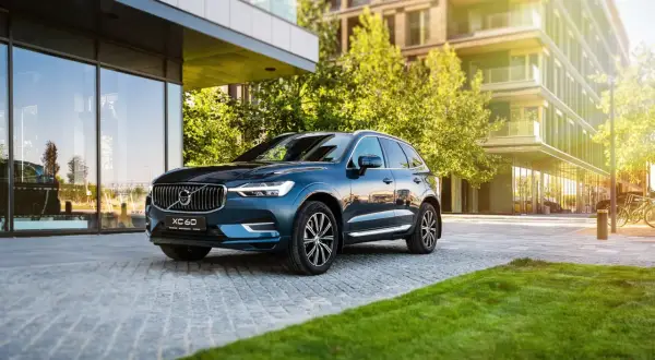 Elegancki, ciemnoniebieski Volvo XC60 zaparkowany przed nowoczesnym budynkiem. Wiele osób szuka volvo xc60 opinie, by podjąć decyzję o zakupie.