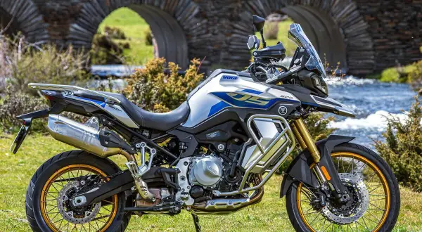 Moto Voge 500DS, una moto china con motor BMW, lista para la aventura junto a un puente de piedra y un río.