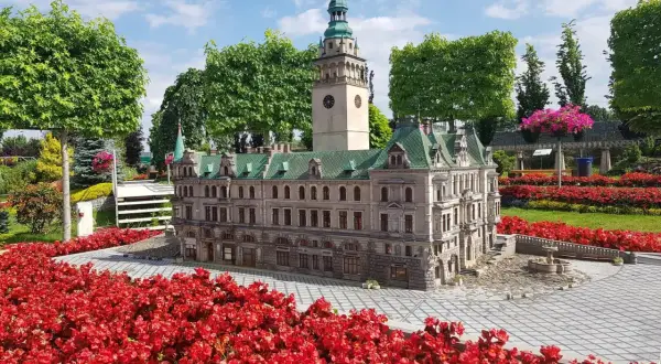 Miniaturowy ratusz z wieżą i zegarem, otoczony czerwonymi kwiatami. Idealne atrakcje dla dzieci Kotlina Kłodzka.