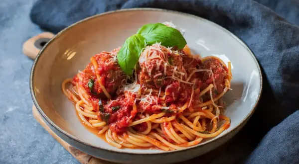 En skål med spaghetti och köttbullar i tomatsås, toppad med parmesan och basilika. En klassisk pasta polpette-rätt.