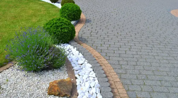 Piękny ogród z zadbanym trawnikiem, kwitnącą lawendą i ozdobnymi krzewami. Ścieżka z kostki brukowej, która wygląda jak po malowaniu, tworzy elegancką całość.
