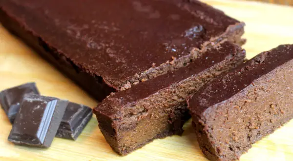Un délicieux gâteau chocolat compote, coupé en tranches, avec des carrés de chocolat à côté.